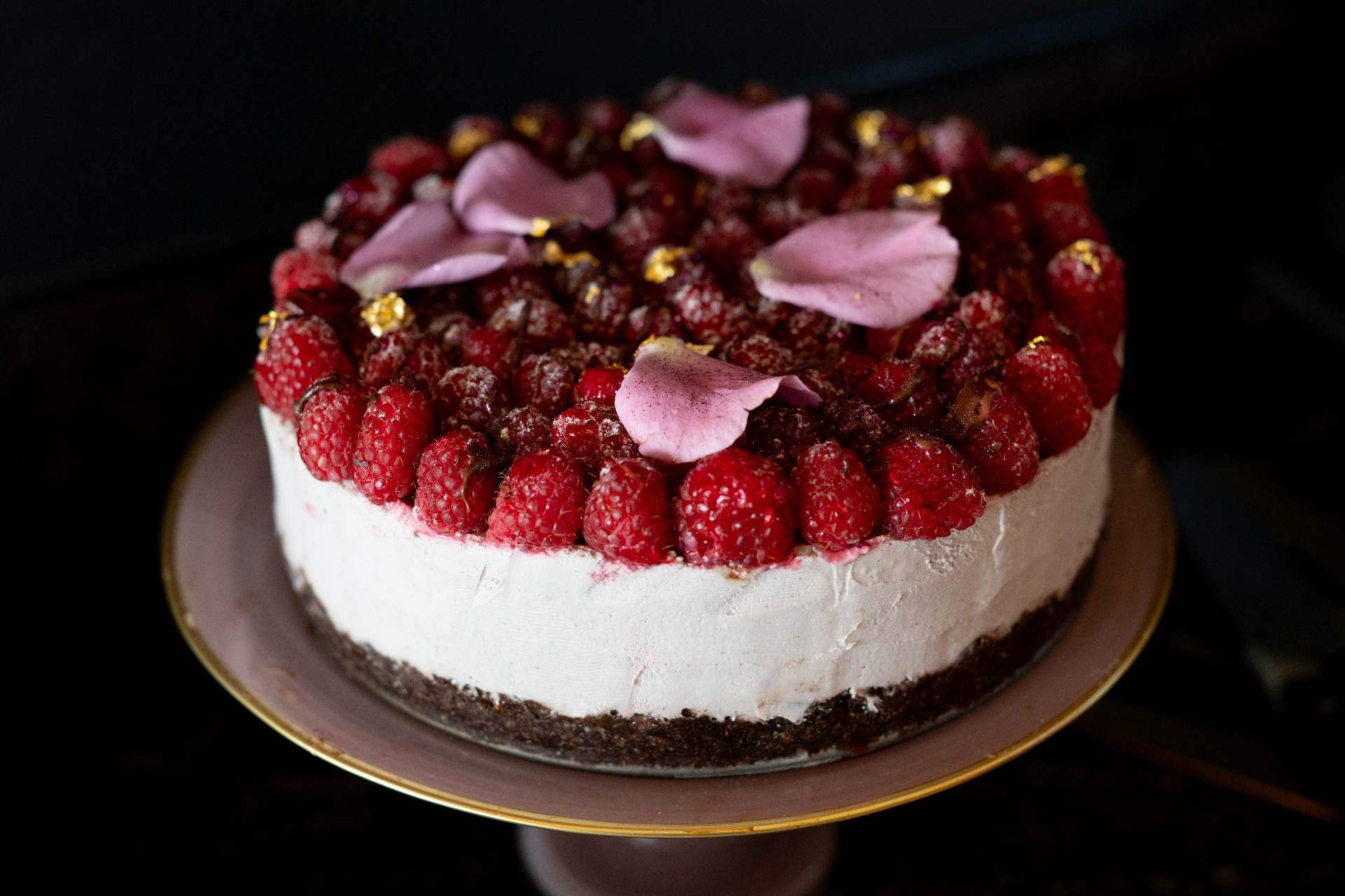 A layered cake crowned with raspberries and rose petals